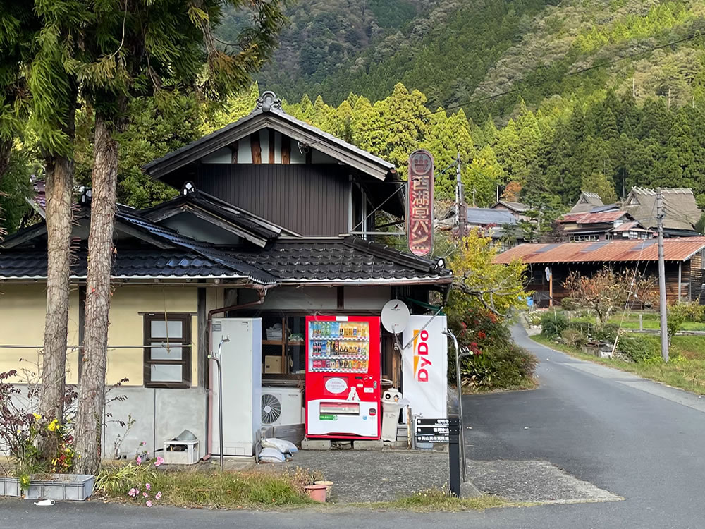 自動販売機とパン屋のノスタルジックな看板が見える美山村落の入口の風景